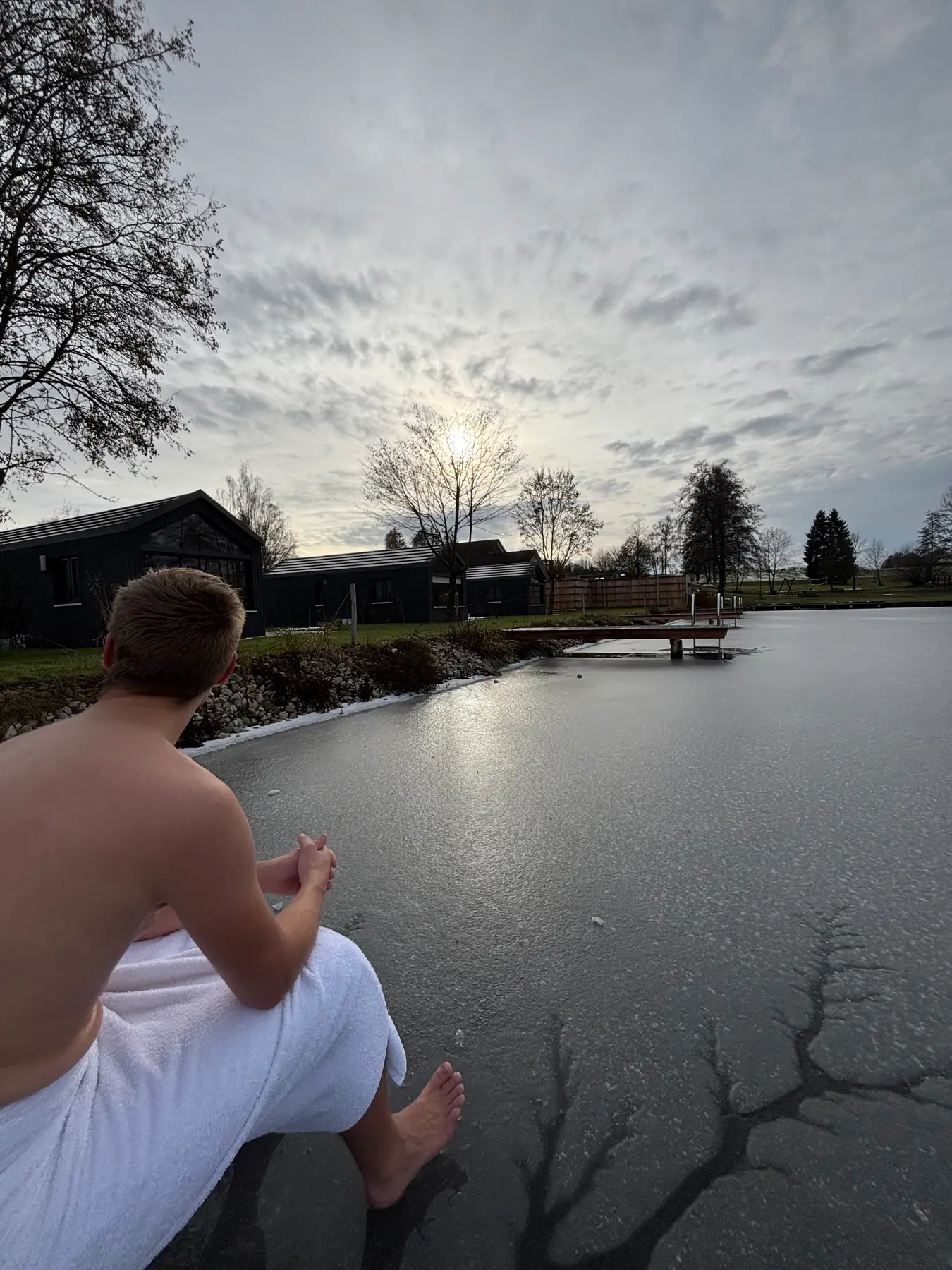 Gast sitzt nach der Sauna am Steg des winterlichen Sees