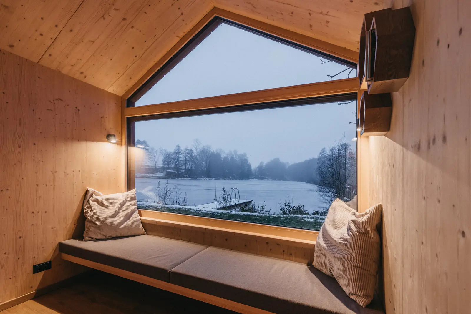 Blick aus dem Panoramafenster einer Cabin auf den verschneiten See
